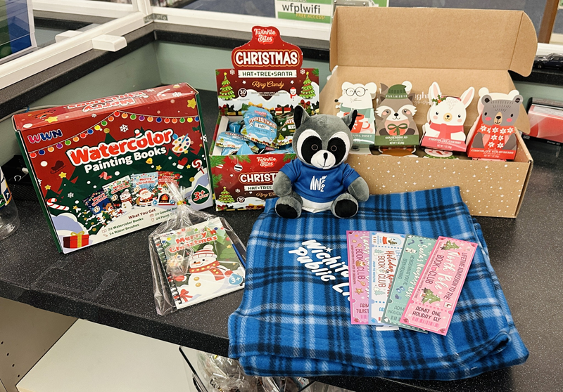 A photograph of winter reading prize items: reading blankets, mascot plush, ring pops, mini watercolor painting book, hot cocoa, and bookmarks