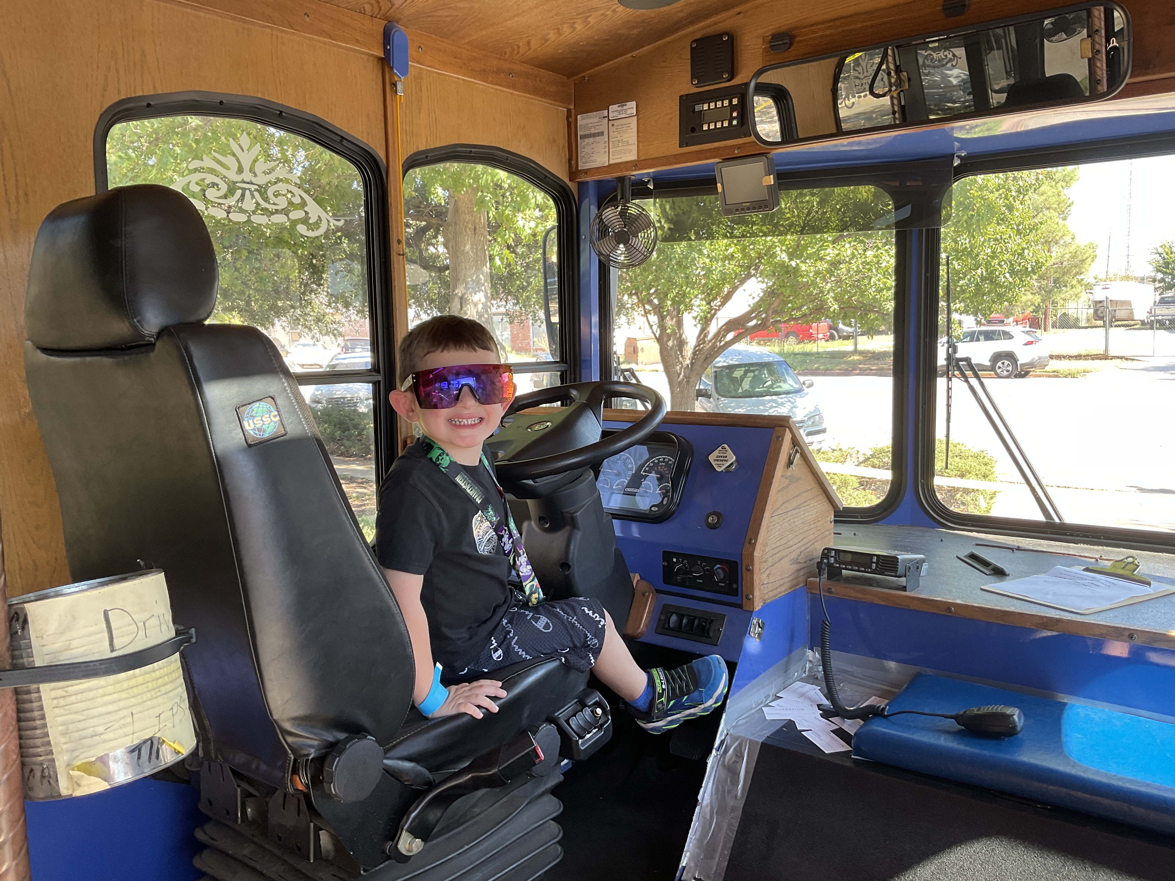 A boy in reflective sunglasses sitting in the driver's seat of the trolley